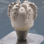 3D-Printed Metal Oil or Water well Drill bit with large industrial machine faded behind it.