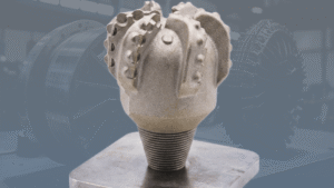 3D-Printed Metal Oil or Water well Drill bit with large industrial machine faded behind it.